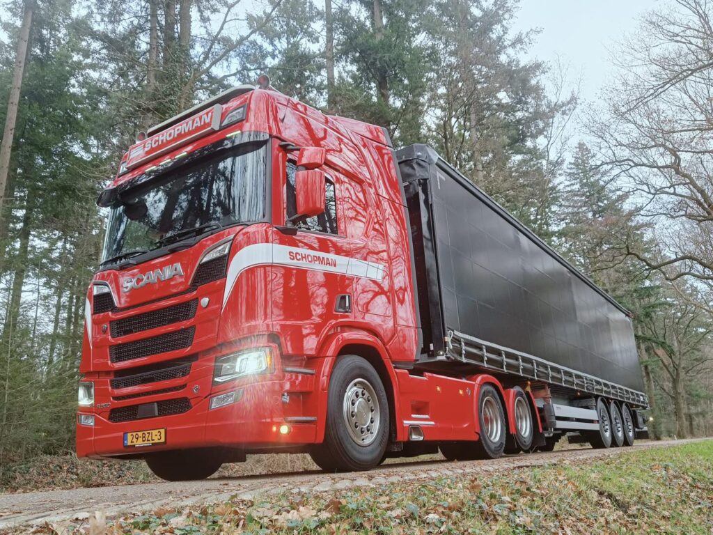 Rode Scania vrachtwagen van Schopman Transport met oplegger op een bosweg