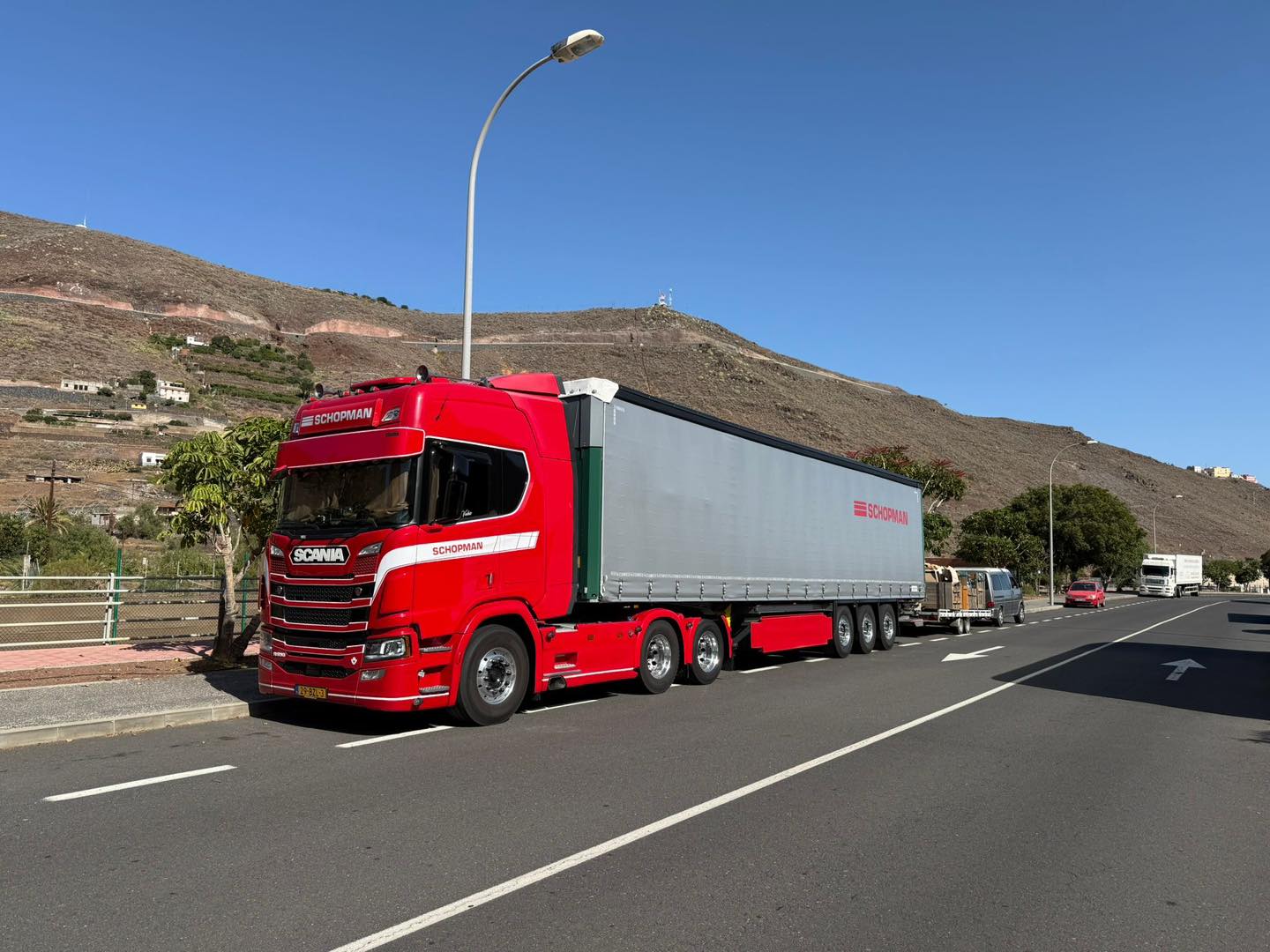 Rode Scania vrachtwagen van Schopman Transport met oplegger geparkeerd langs een weg in een bergachtig landschap
